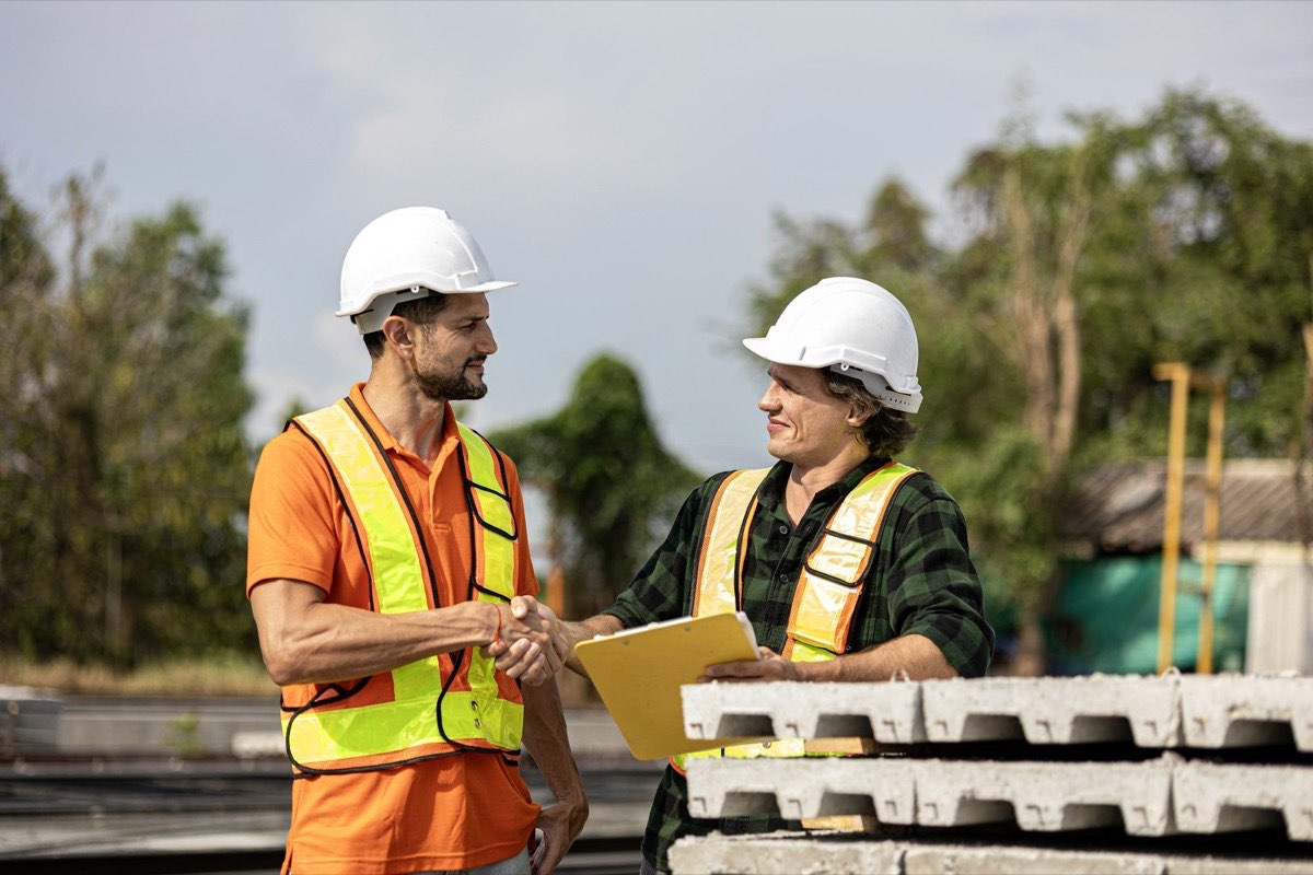 Dos profesionales estrechando manos en una obra en construcción con planos